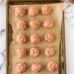 top view of rows of raw Italian meatballs on a parchment lined tray