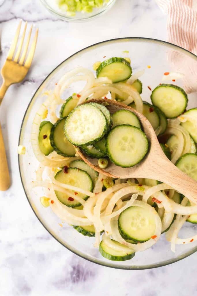 slices of cucumber and spices in a mixing bowl for korean cucumber salad