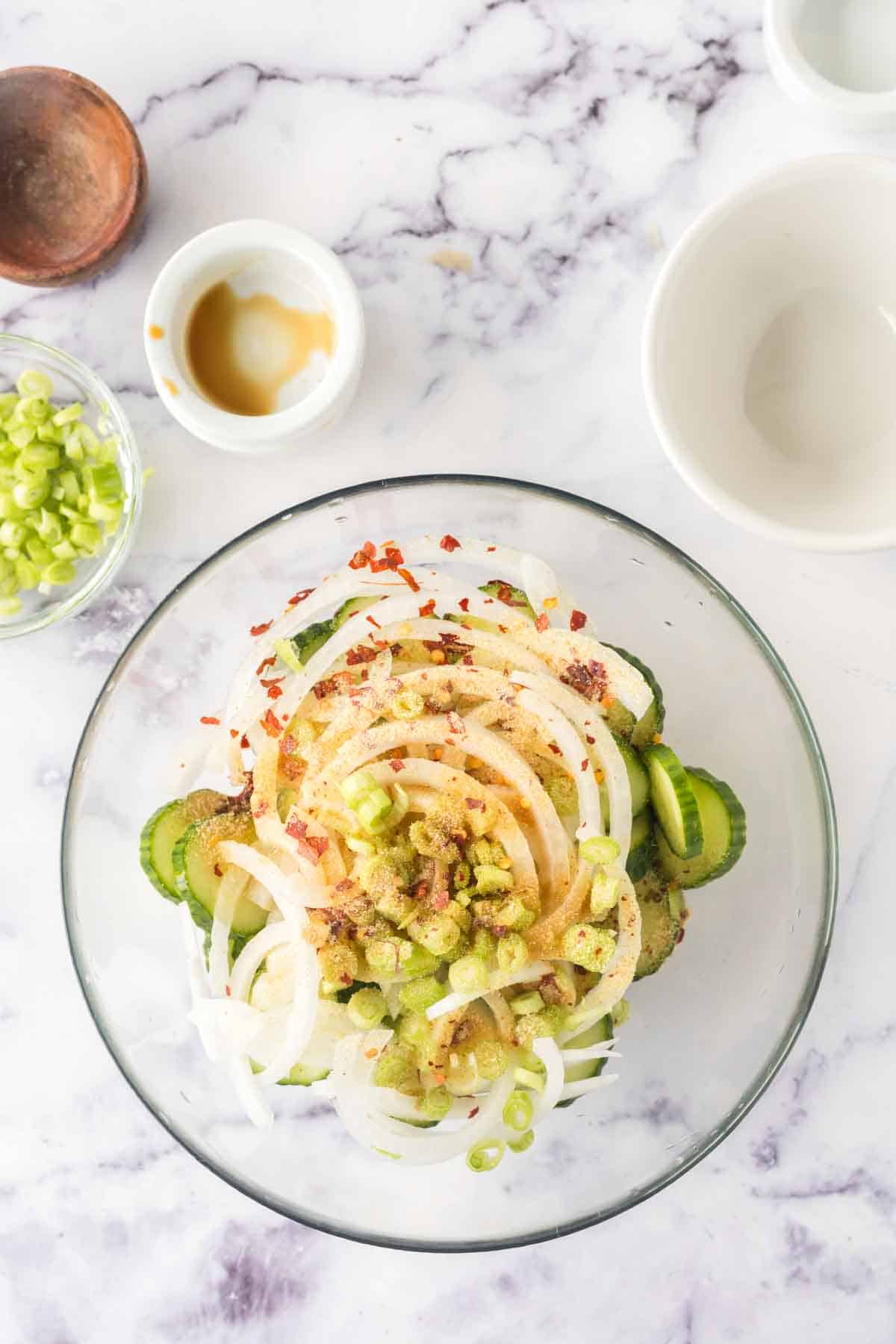 slices of cucumber and spices in a clear mixing bowl for korean cucumber salad