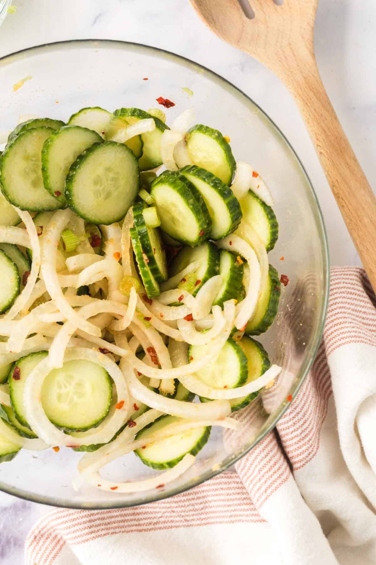 slices of cucumber and spices in a clear mixing bowl for korean cucumber salad