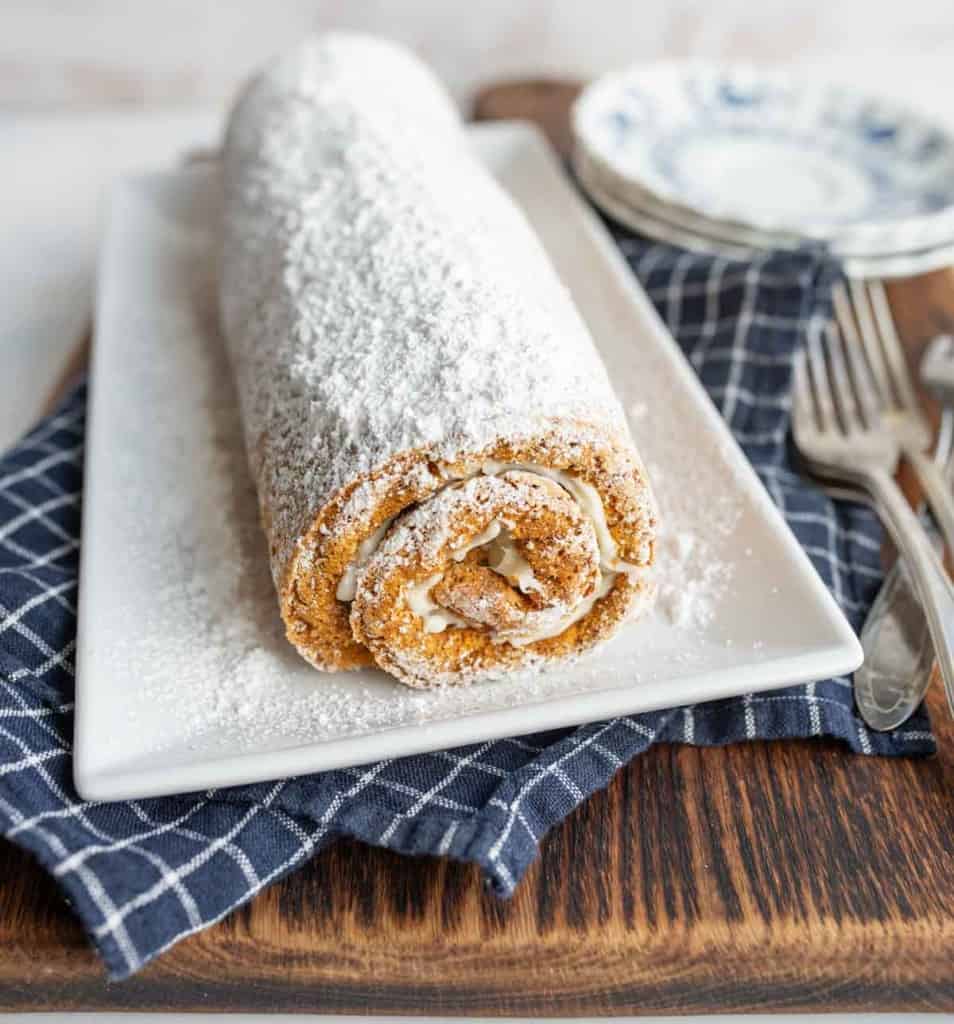 pumpkin cake roll whole on a long plate with sugar on top