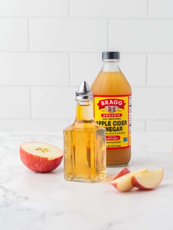 glass pouring dish and a bottle of apple cider vinegar with sliced apples