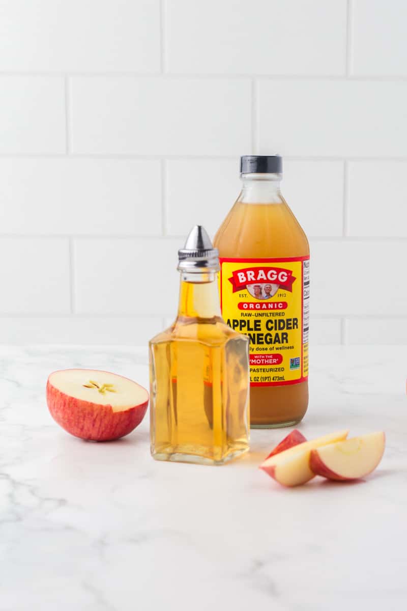 glass pouring dish and a bottle of apple cider vinegar with sliced apples