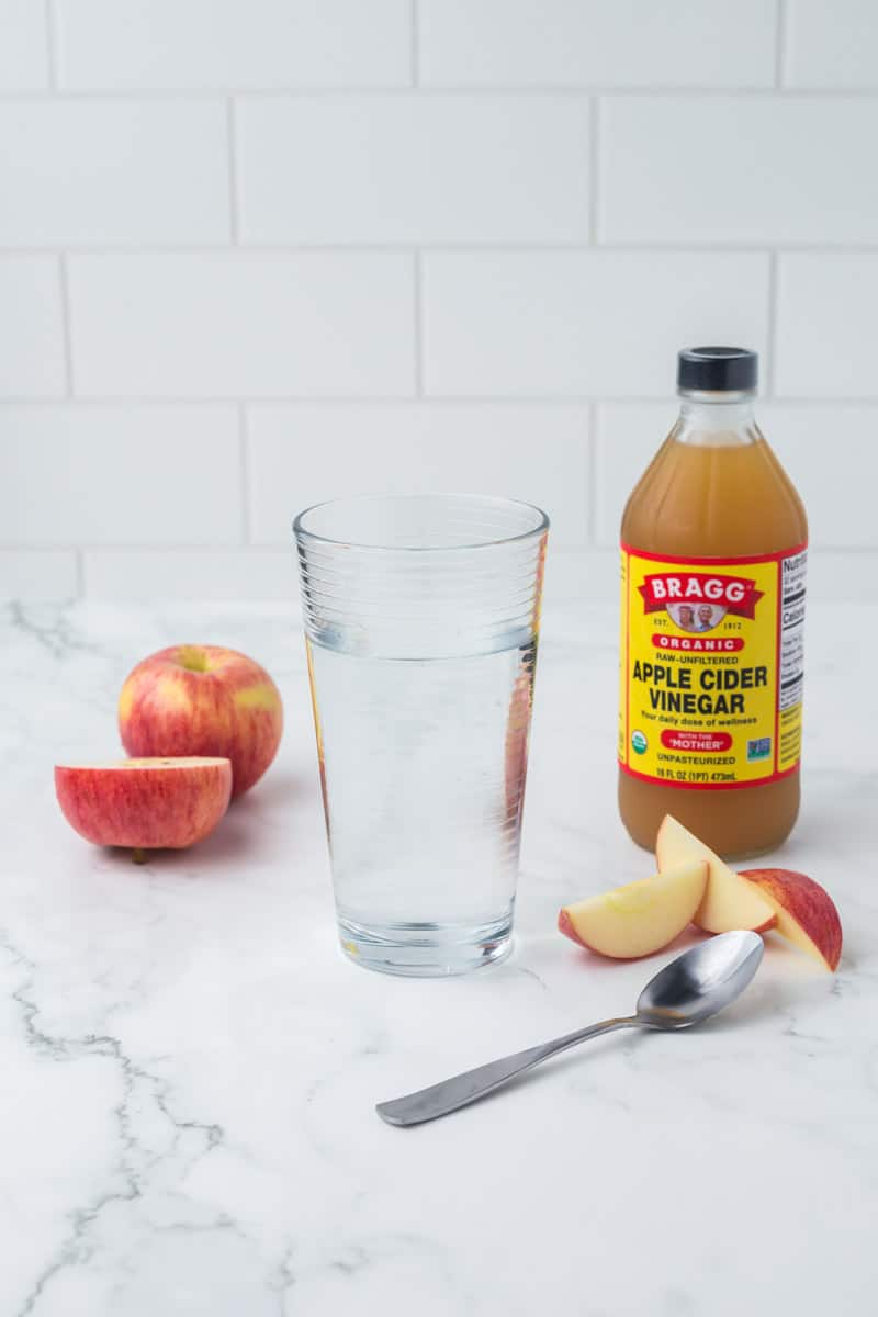 glass bottle of BRAGG organic apple cider vinegar a pint glass and sliced apples