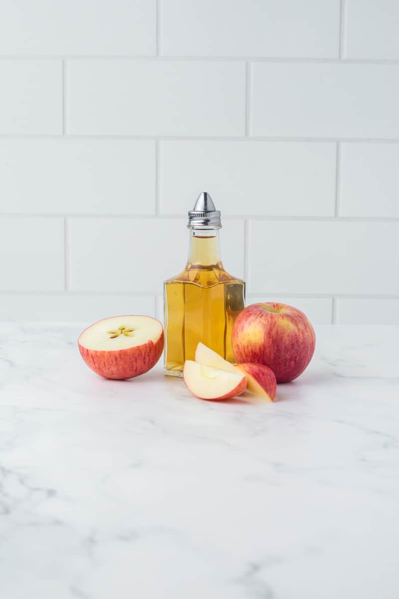 glass pouring dish of apple cider vinegar with sliced apples