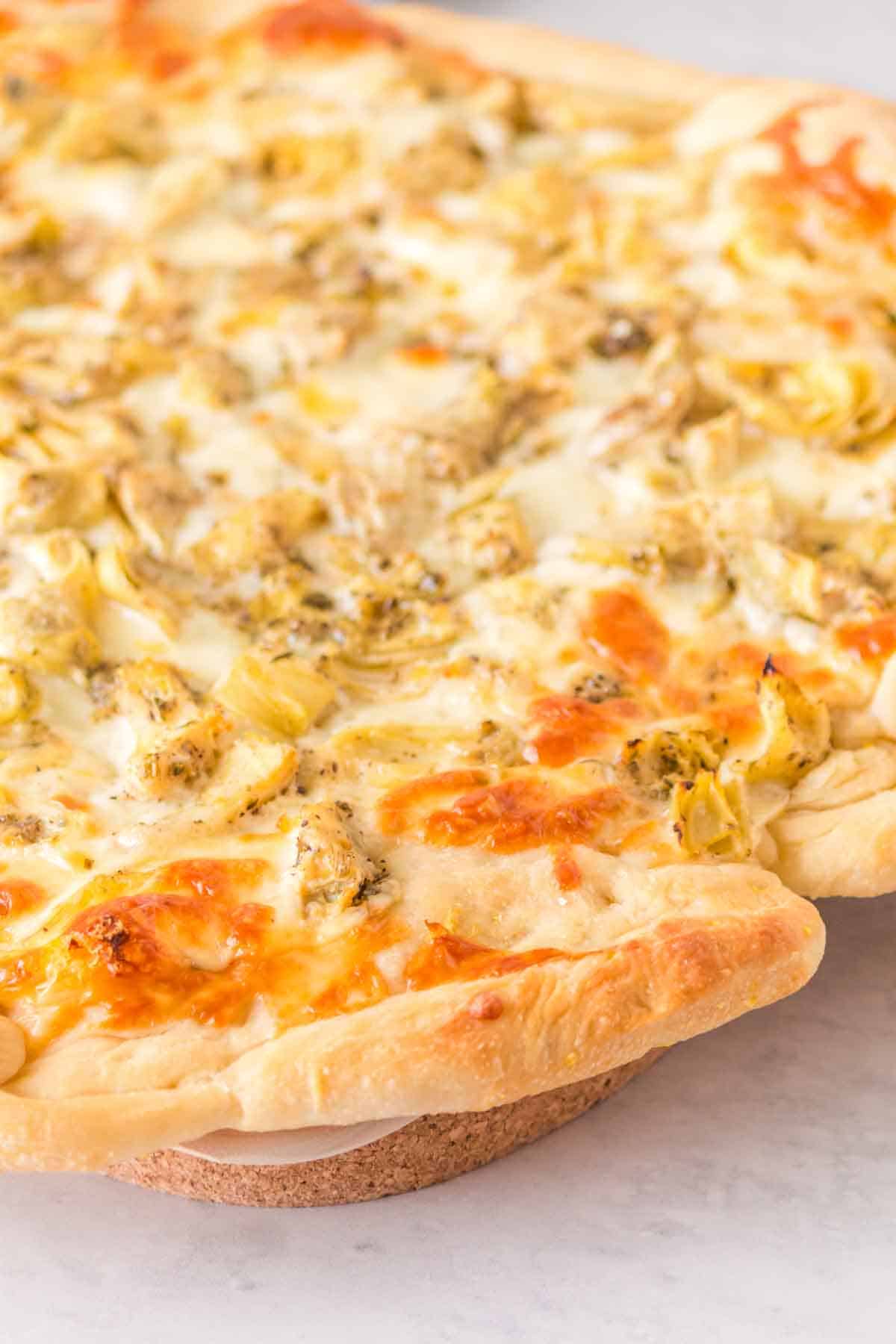 close up of baked artichoke pizza on a wooden paddle