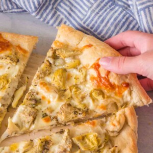 POV hand holding a slice of artichoke pizza