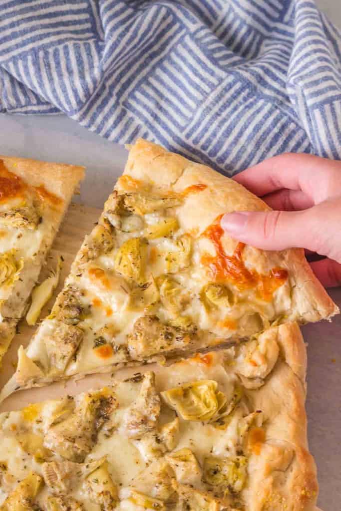 POV hand holding a slice of artichoke pizza