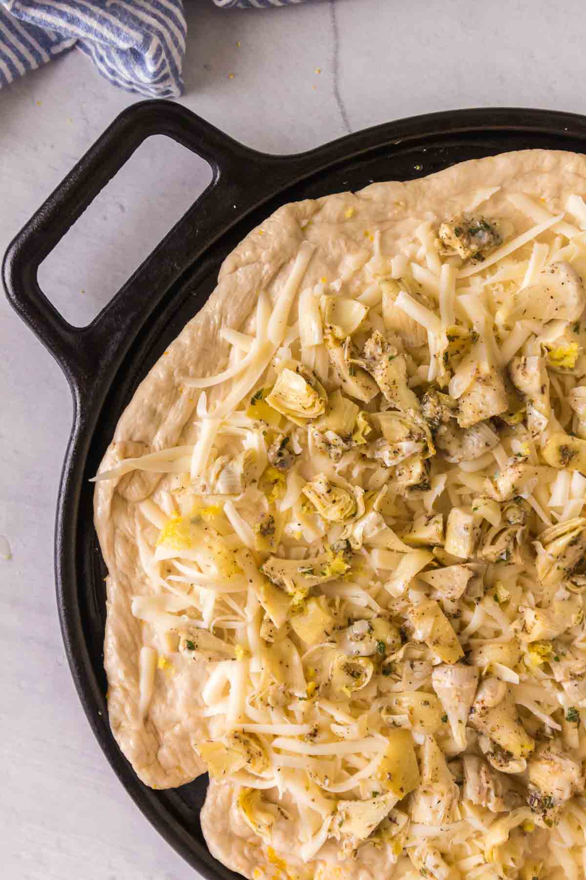 artichoke pizza on a cast iron pan before being baked