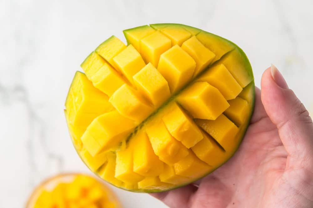 POV hand holding a cube cut mango