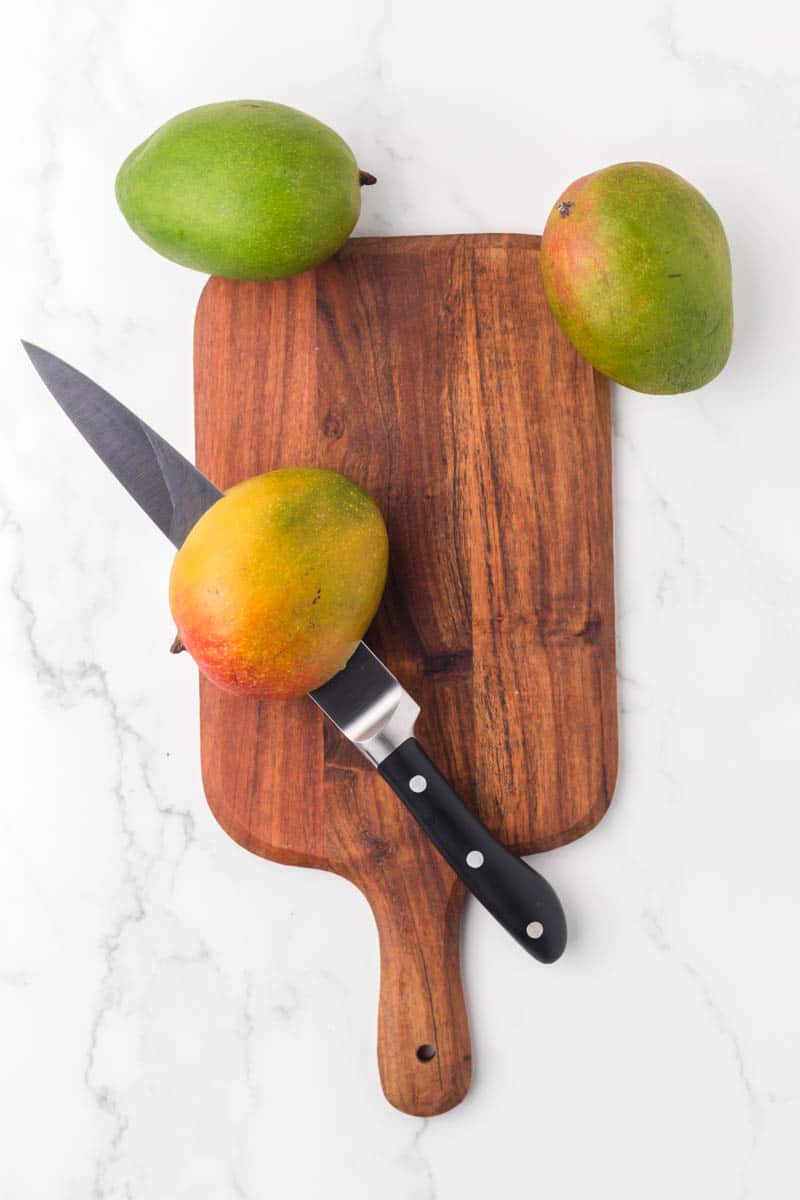 whole fresh mangos on a cutting board