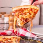 POV hand with spatula pulling a cut slice of pineapple pizza from the pan