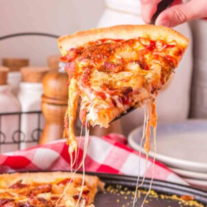 POV hand with spatula pulling a cut slice of pineapple pizza from the pan