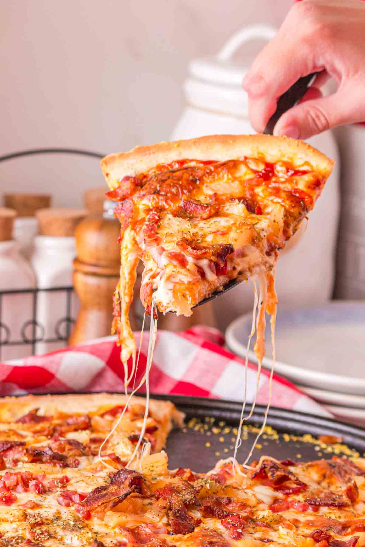 POV hand with spatula pulling a cut slice of pineapple pizza from the pan