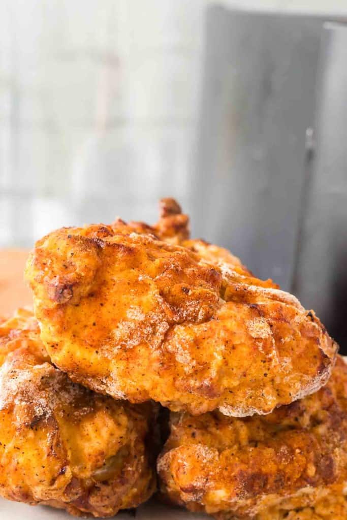 close up of crispy golden skin on three pieces of air fryer fried chicken stacked on a plate