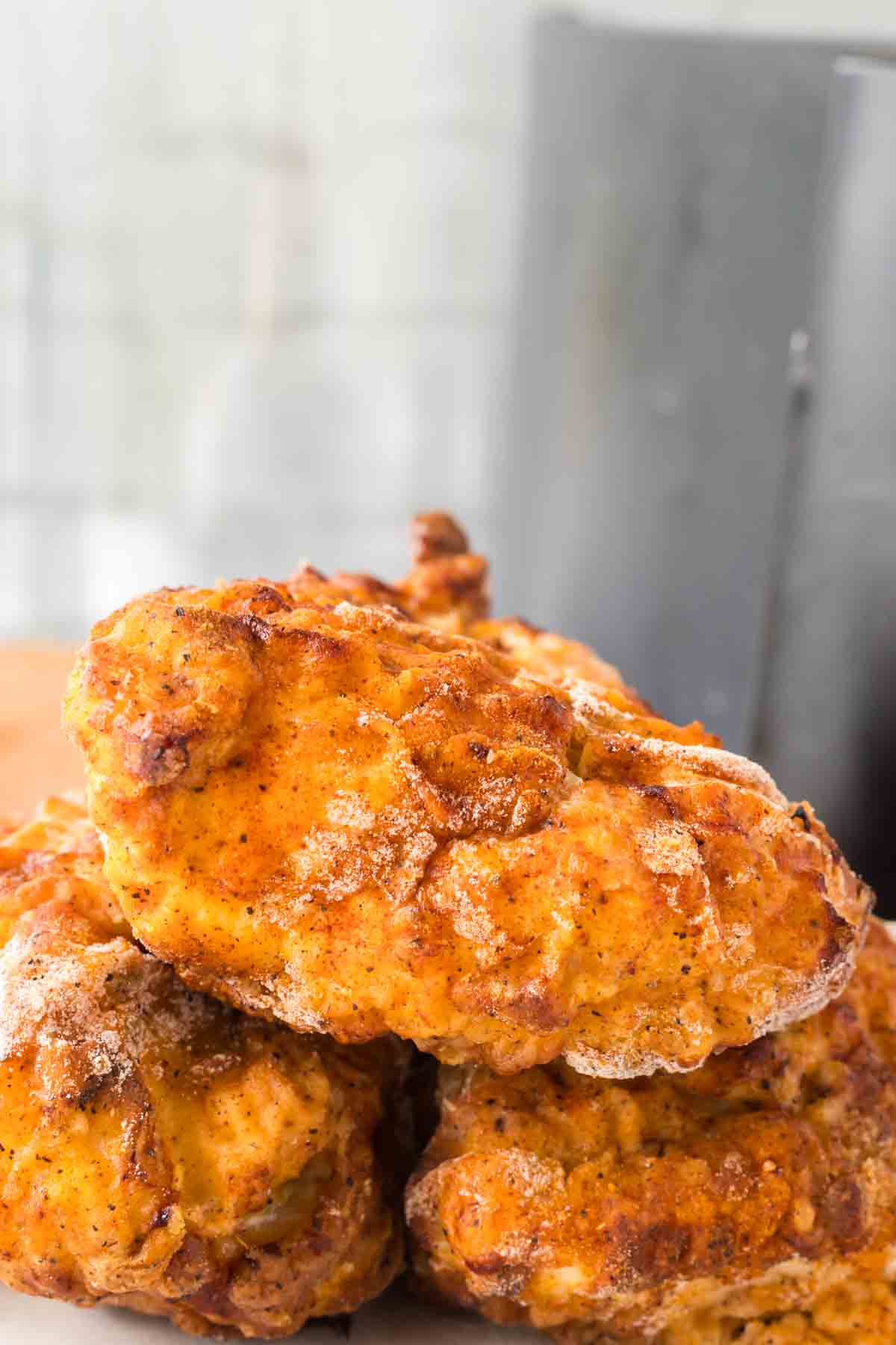 close up of crispy golden skin on three pieces of air fryer fried chicken stacked on a plate