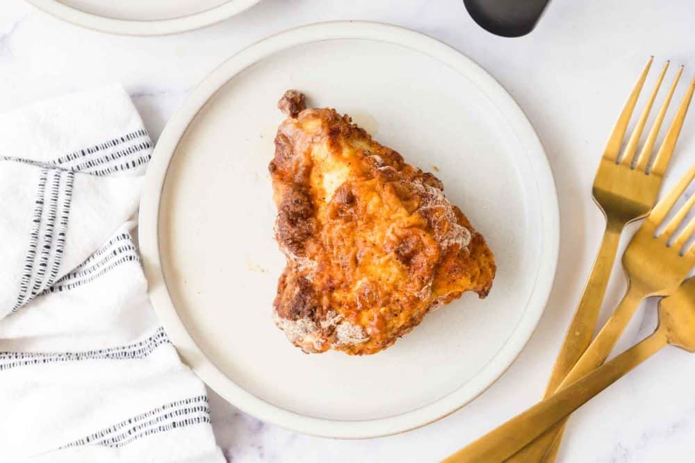 one pieces of air fryer fried chicken on a plate with golden forks.