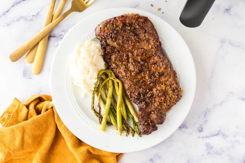 top view of a plated air fryer steak plated next to asparagus and mashed potatoes.