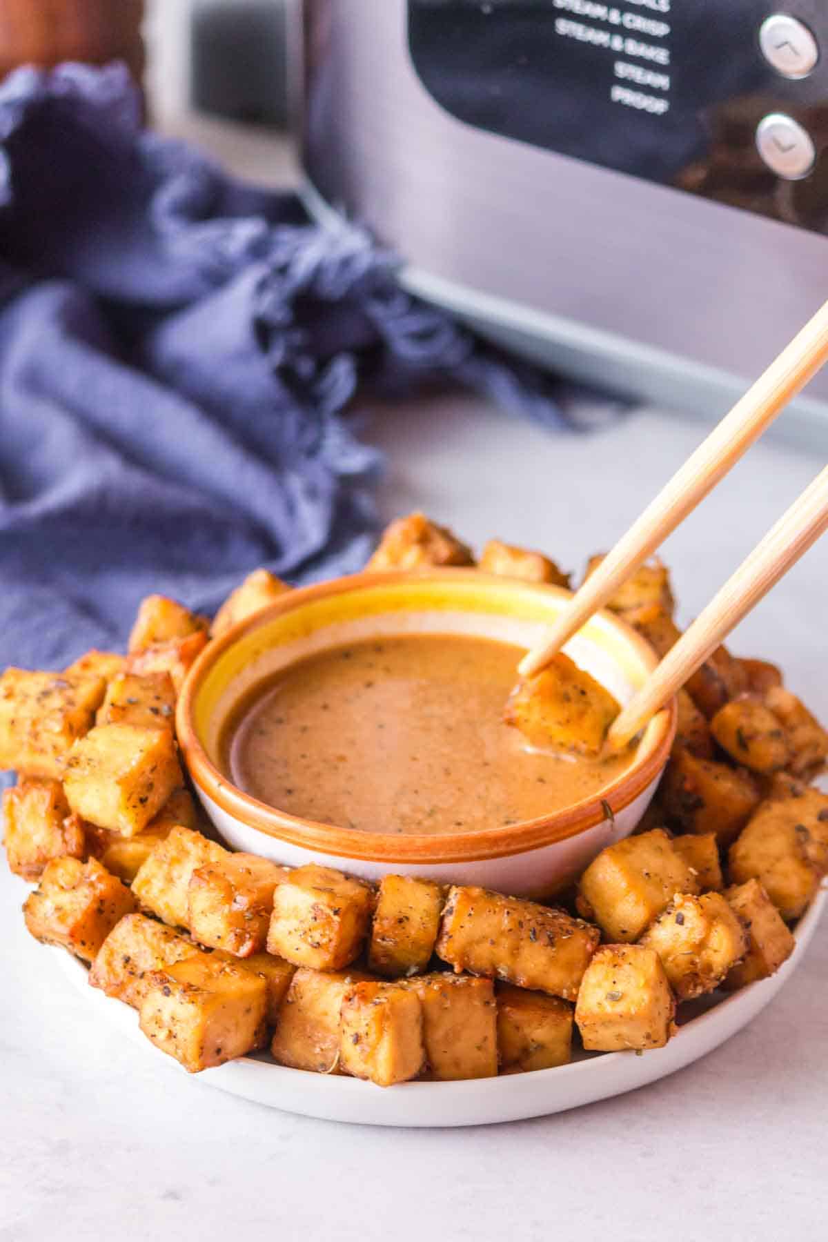 POV chopsticks dipping into a plate of air fryer tofu with a dish of sauce in the center