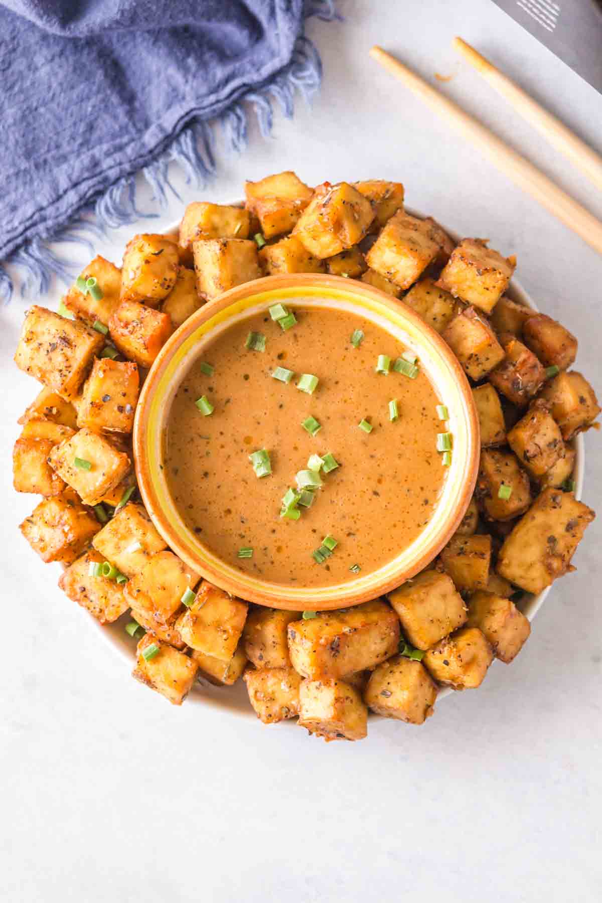 top view of a plate of air fryer tofu with a dish of dipping sauce in the center.