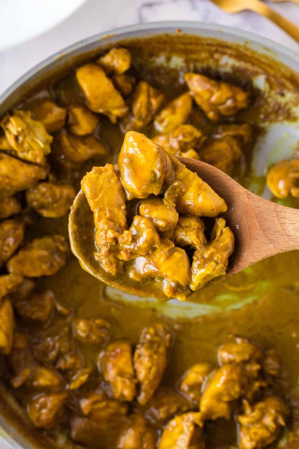 pan full of coconut chicken curry in sauce with a wooden spoon