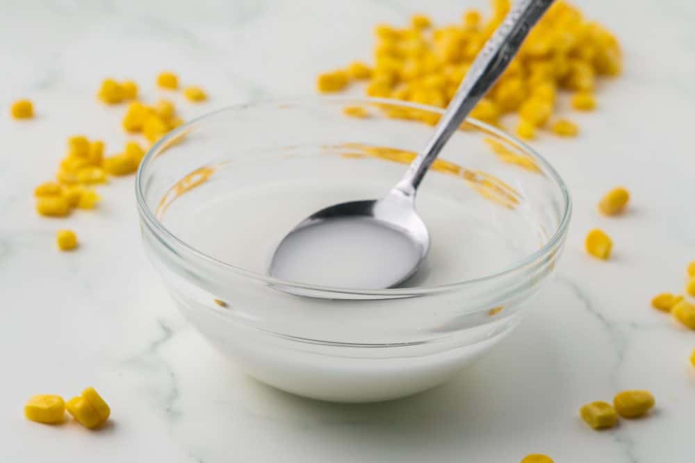 corn starch slurry bowl with a bottle of corn starch and corn kernels all around
