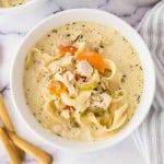 top view of a white bowl of creamy chicken noodle soup and a golden spoon