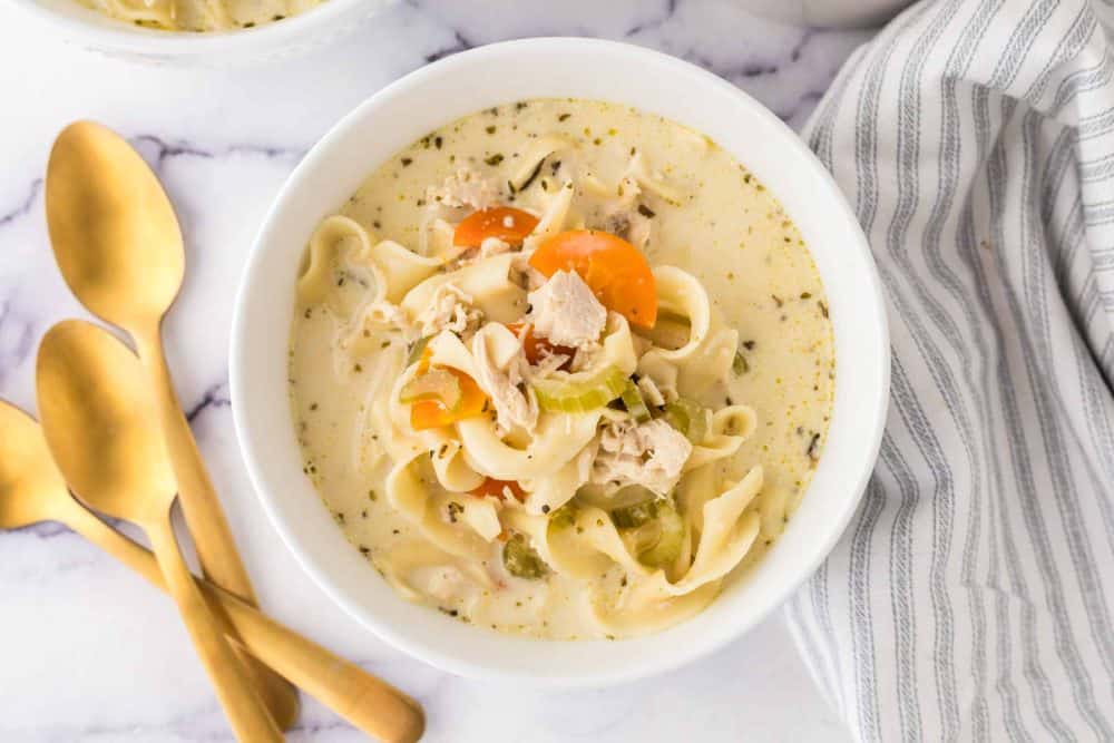 top view of a white bowl of creamy chicken noodle soup and a golden spoon