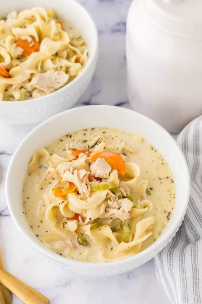 top view of a white bowl of creamy chicken noodle soup and a golden spoon