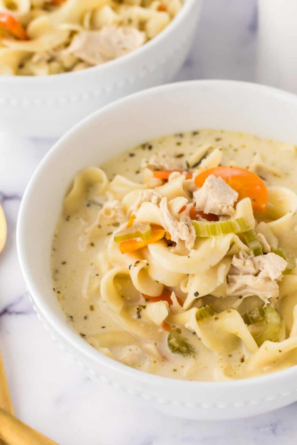 close up of white bowl of creamy chicken noodle soup and a golden spoon