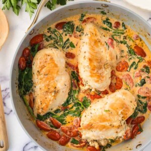 creamy tuscan chicken recipe with a whole breast in sauce inside a pot