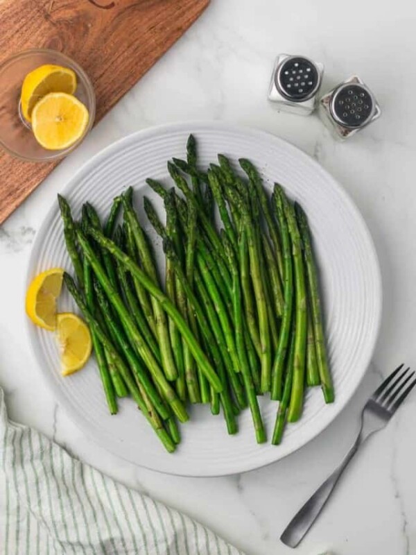 top view of a round white plate with sautéed asparagus and lemon on the side