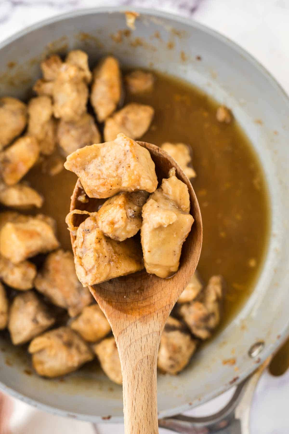 wooden spoon scooping chicken cubes in a saucepan