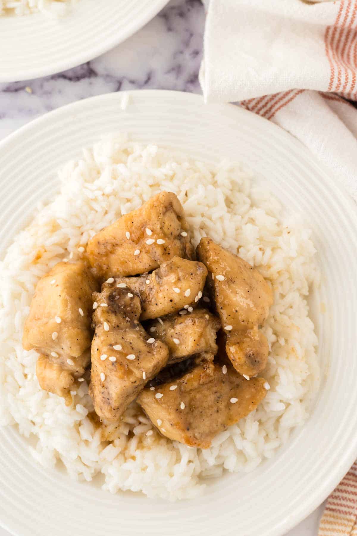 top view close up of honey chicken cubes over rice on a white plate