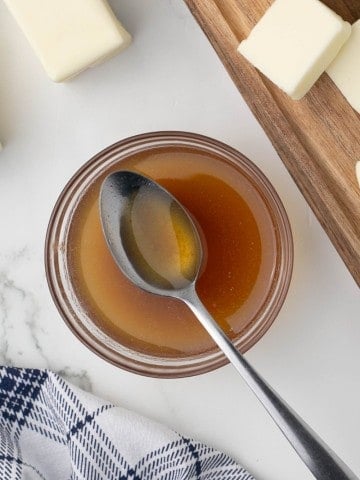 a clear glass bowl of melted brown butter and a spoon in an aesthetic photo