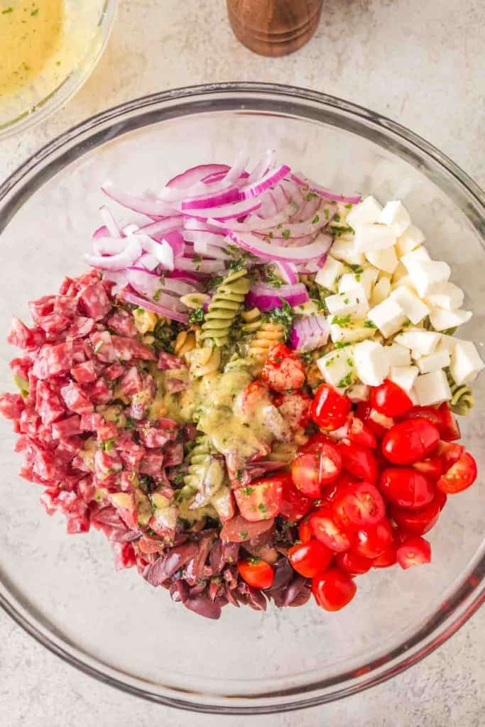ingredients for Italian pasta salad in a clear mixing bowl