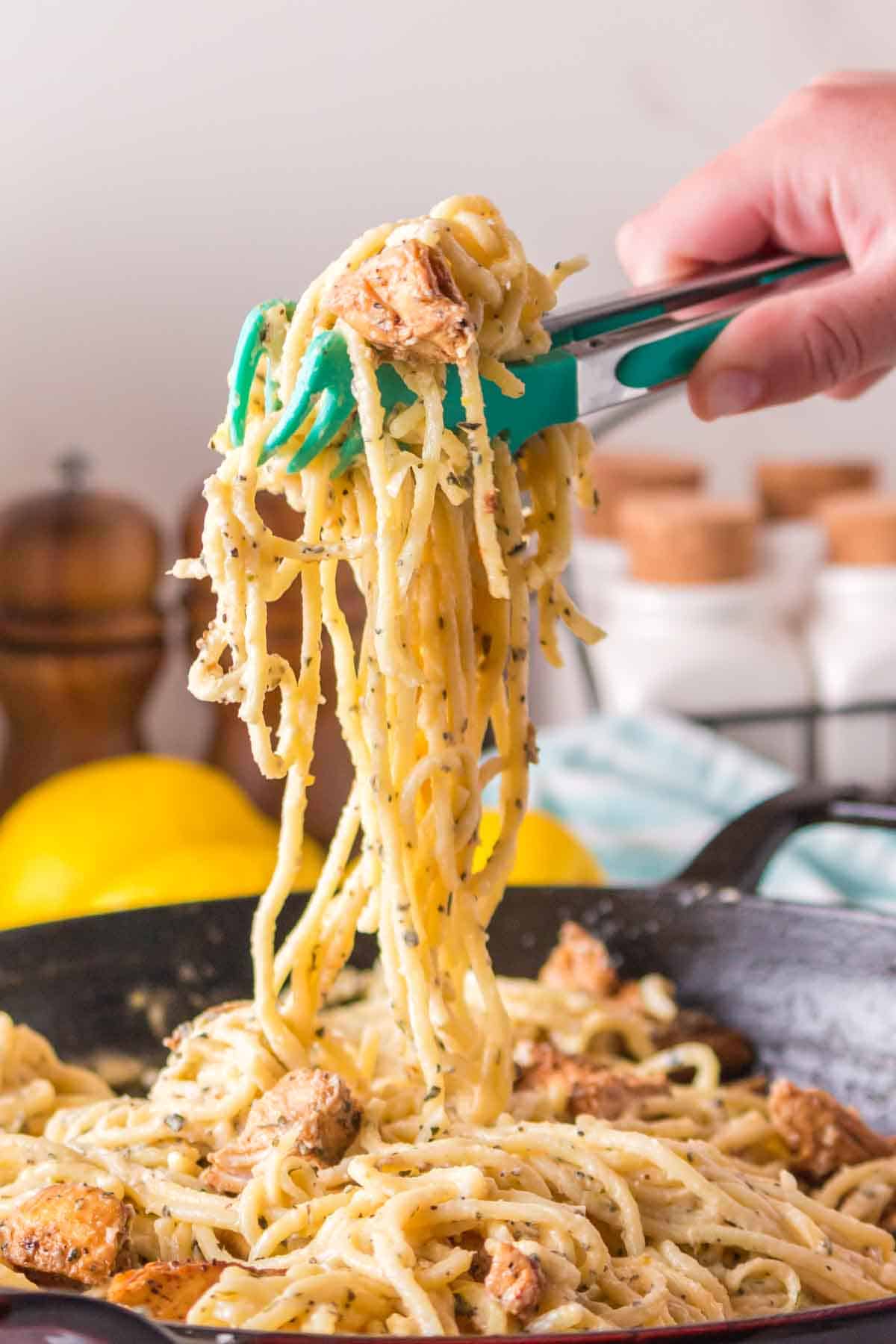 POV hand holding tongs with lemon chicken pasta