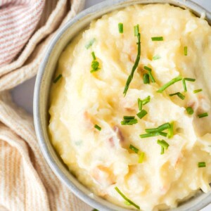 loaded mashed potatoes in a small serving bowl with golden spoons