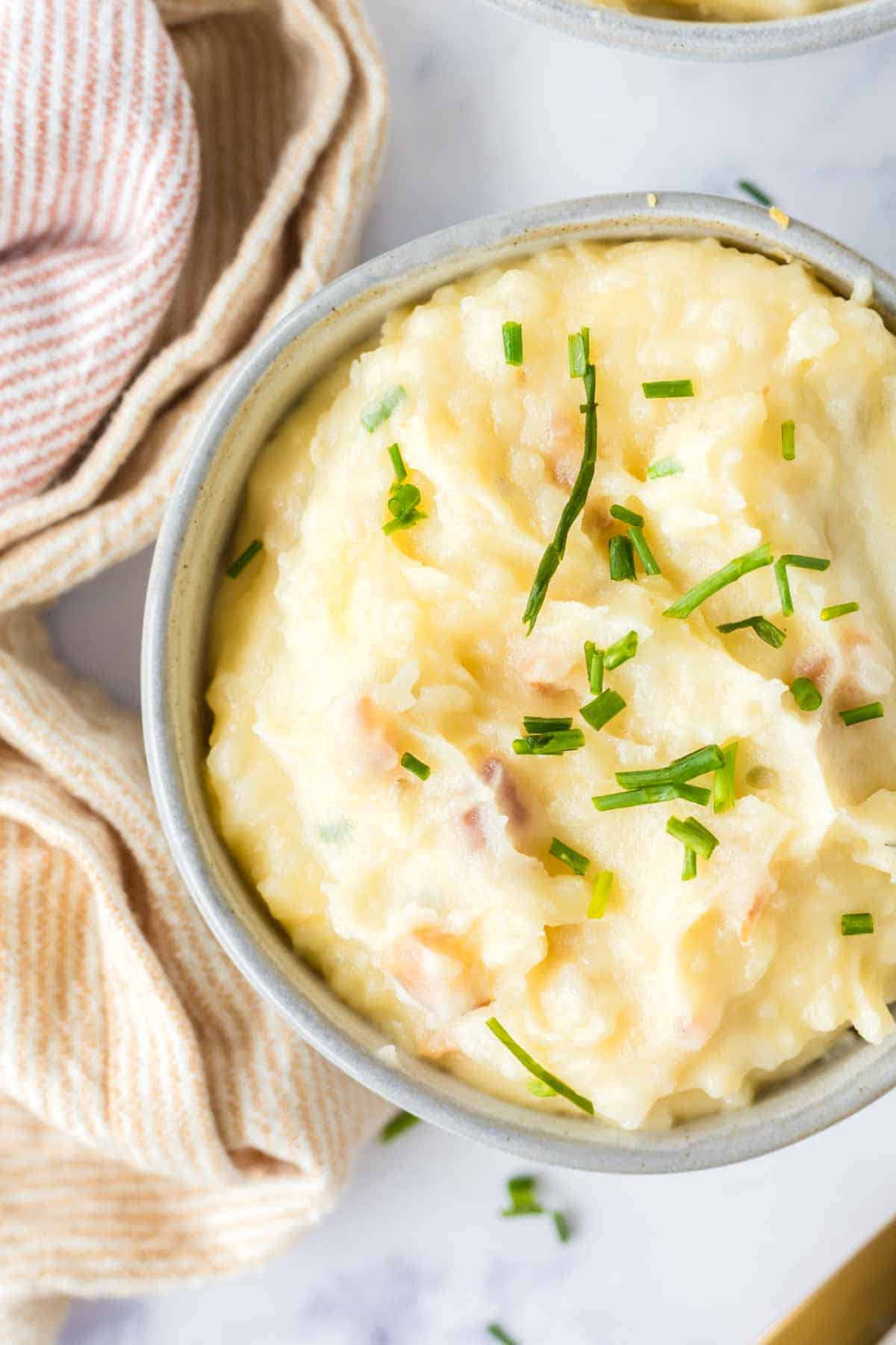 loaded mashed potatoes in a small serving bowl with golden spoons