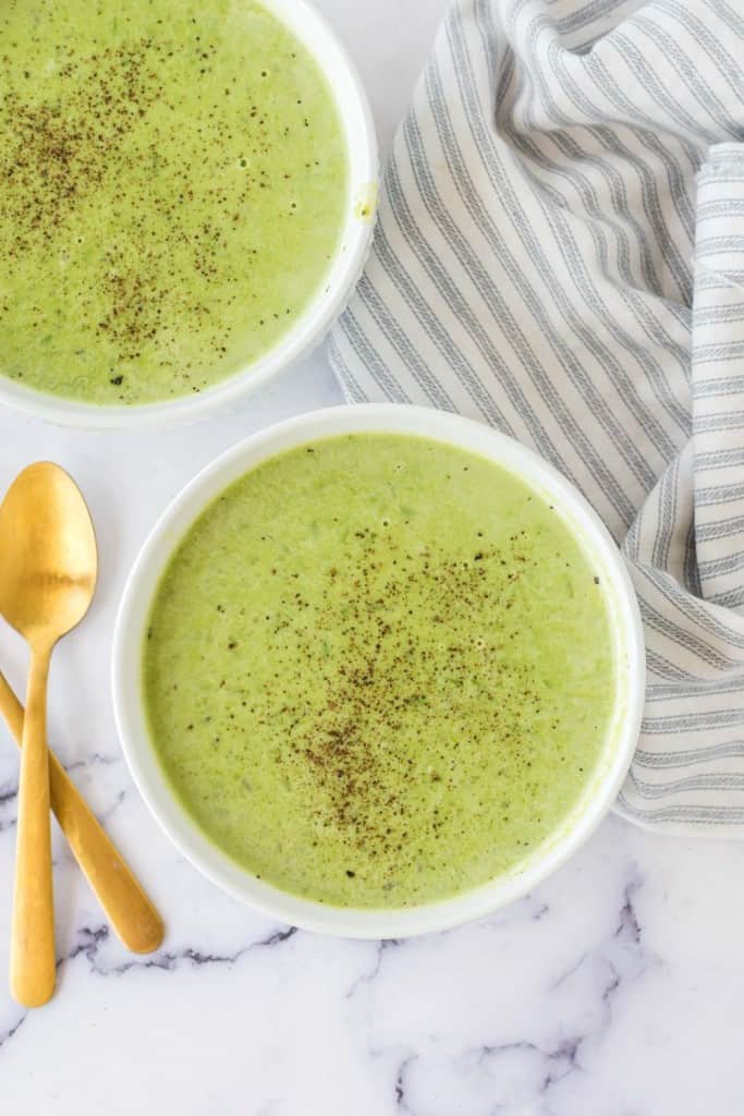 vibrant green pea soup in serving bowls with pepper on top