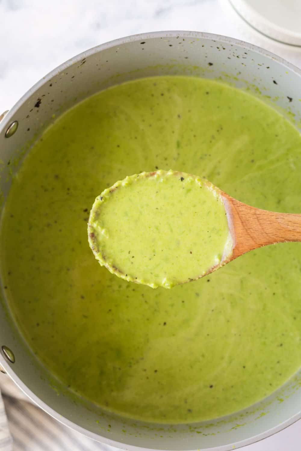 vibrant green pea soup on a wooden spoon in a pot