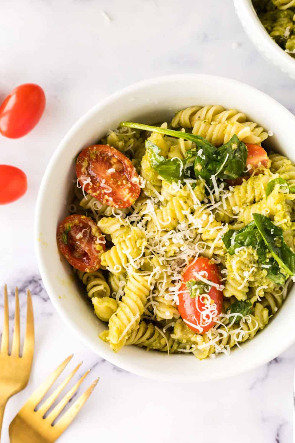 top view of a portion bowl of pesto pasta salad with shredded parmesan cheese