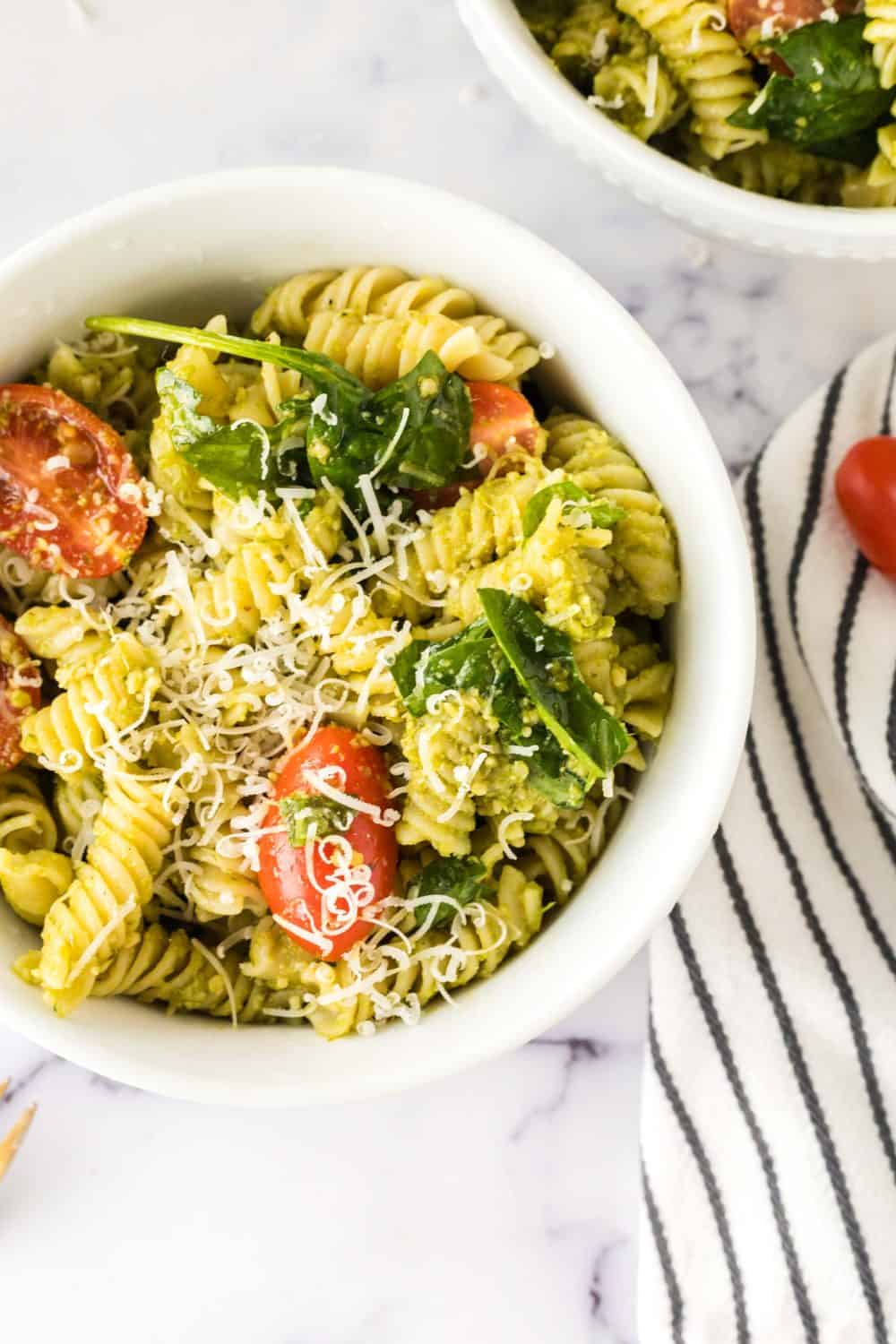 portion bowl of pesto pasta salad with shredded parmesan cheese