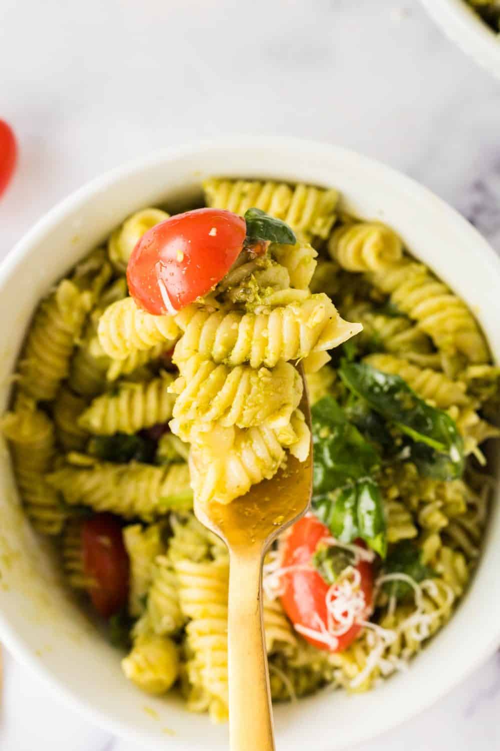 top view of a forkful of a portion bowl of pesto pasta salad with shredded parmesan cheese