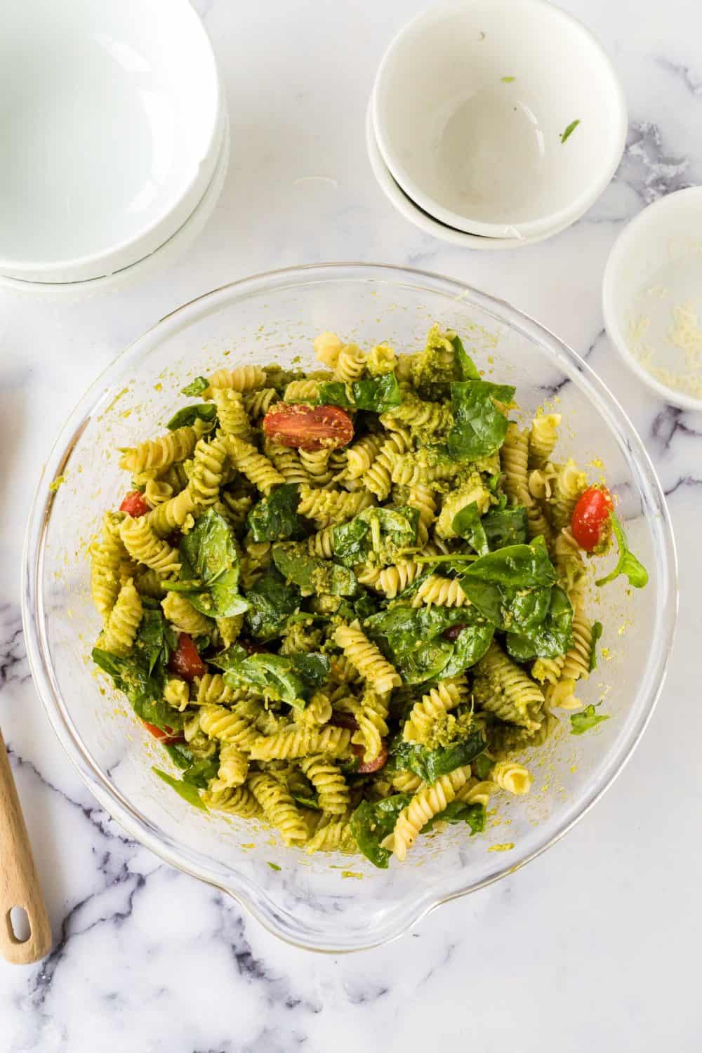 top view of a clear mixing bowl with pesto pasta salad