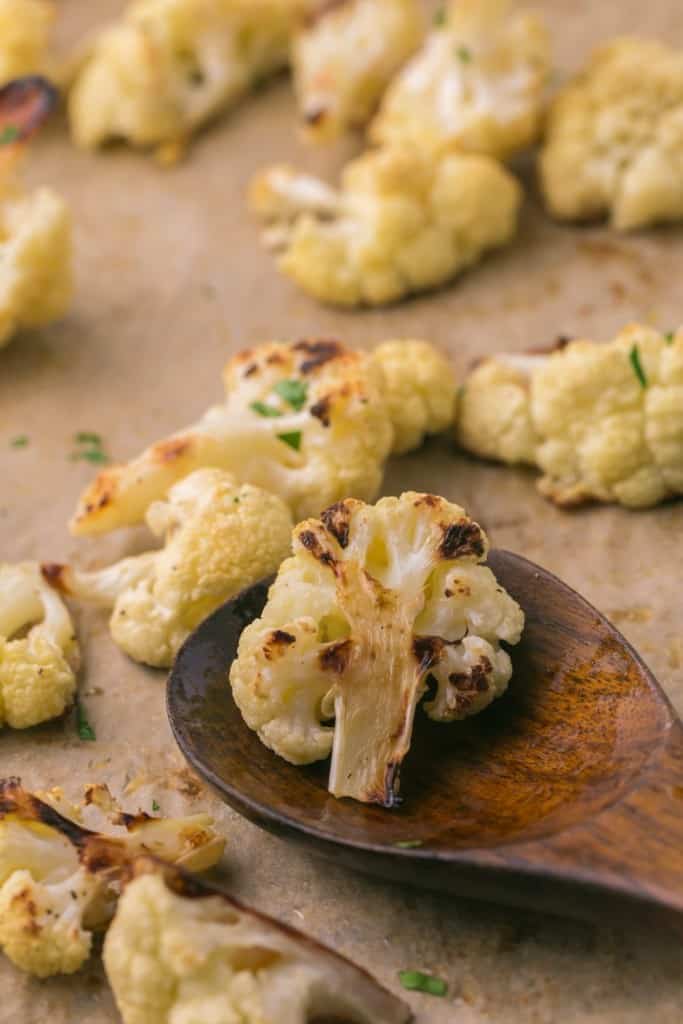 a baking dish with seasoned roasted cauliflower on a wooden spoon