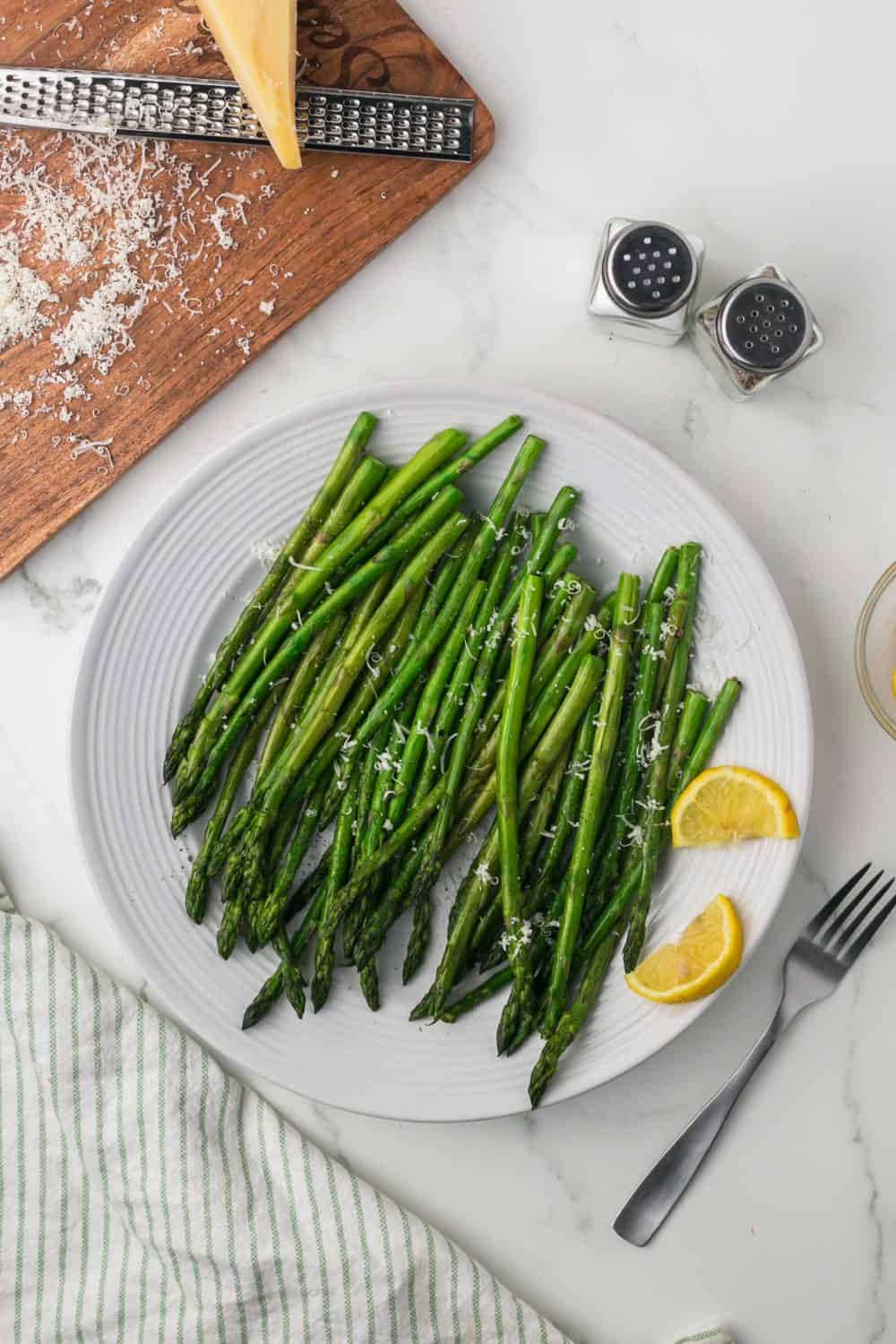 top view of a round white plate with sautéed asparagus with parmesan cheese and lemon on the side