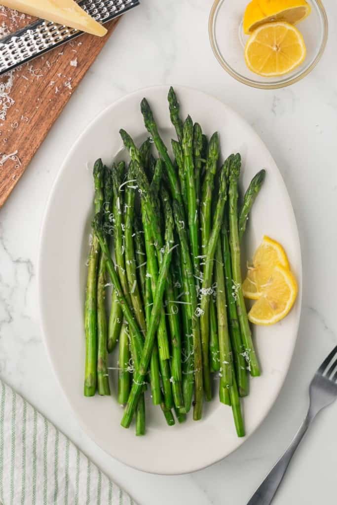 a white plate with sautéed asparagus with parmesan cheese and lemon on the side featured in vegetable recipes for spring.