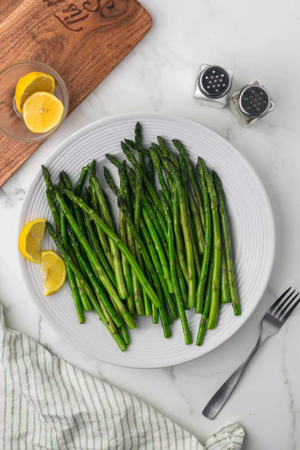 top view of a round white plate with sautéed asparagus and lemon on the side