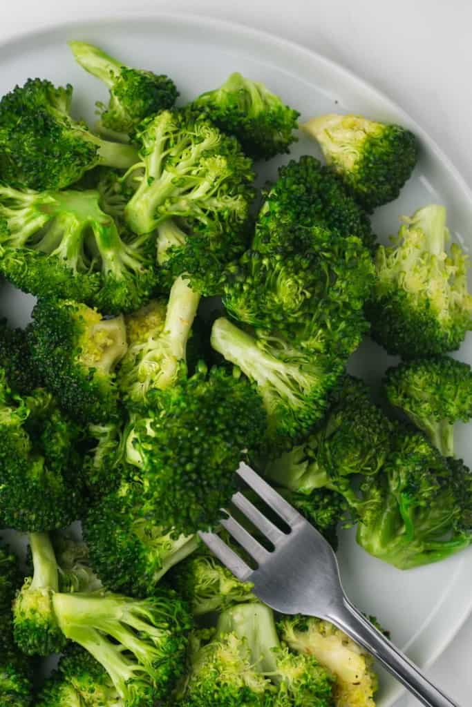 close up of view of a round white plate of sautéed broccoli and a fork